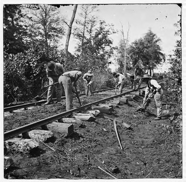 Track maintenance. This is T-rail, with a spike at each tie. Notice that the ties are laid in the dirt.